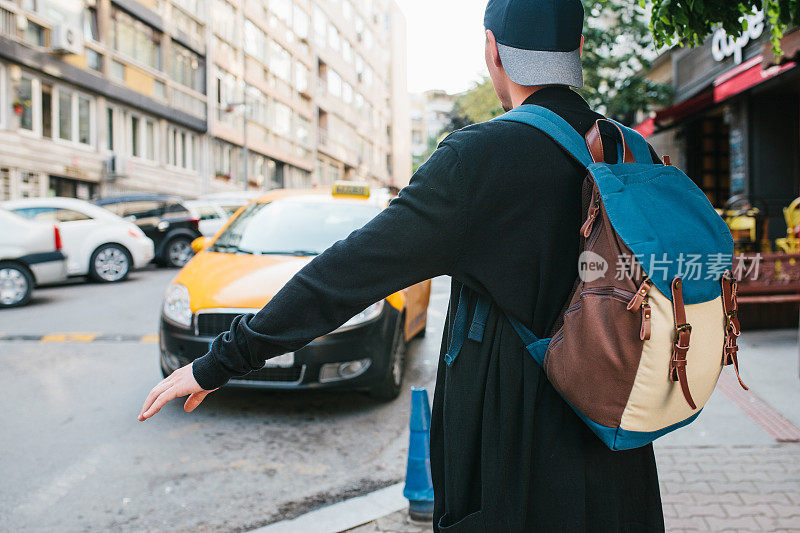 一个背着背包的年轻男游客正在大城市里等出租车。的旅程。观光。旅行。