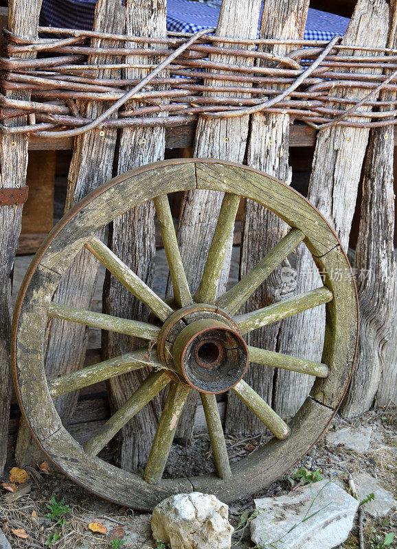 用木板和树枝做成的篱笆墙旁的旧木制车轮