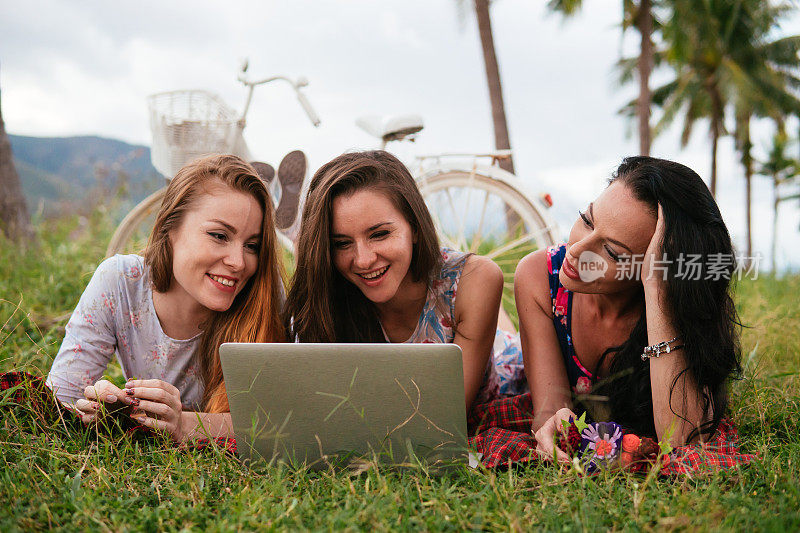 在乡村野餐时，妇女们躺在草地上一起使用笔记本电脑