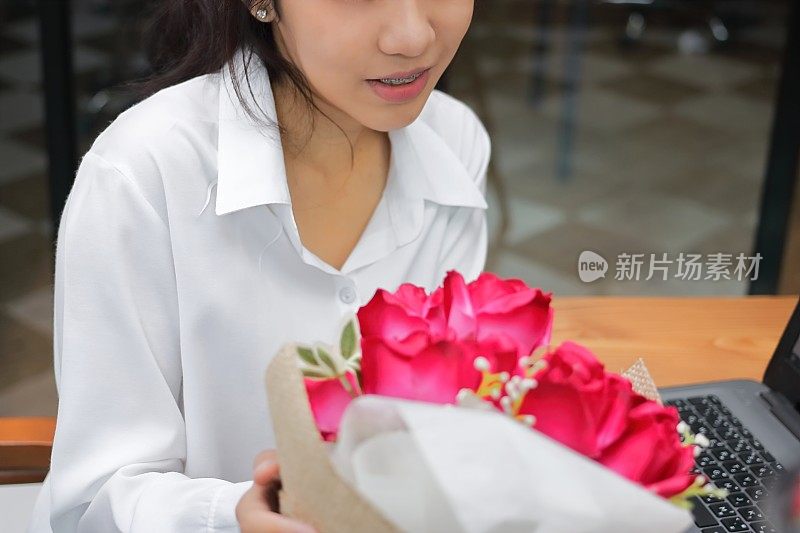 在情人节，一名快乐的年轻亚洲女子从男友那里接过一束红玫瑰。职场爱情和浪漫的概念。