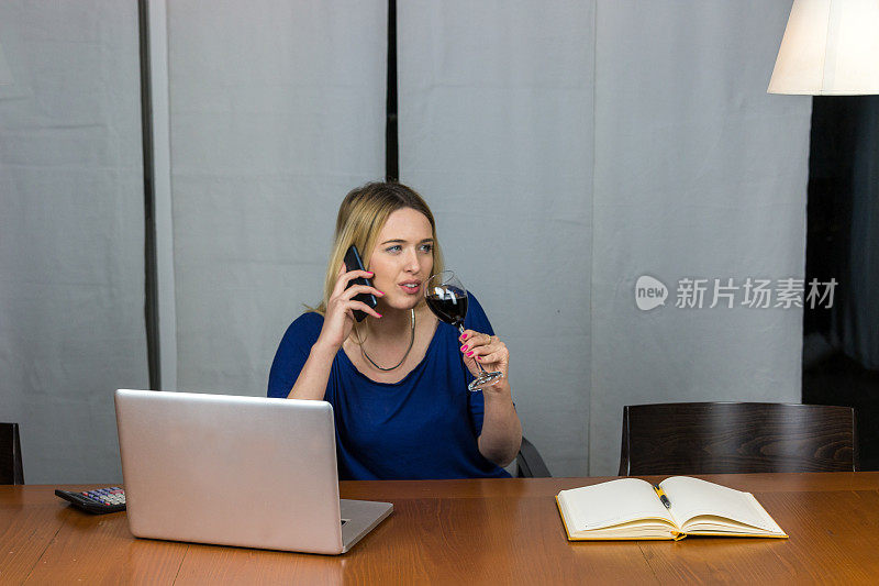 漂亮的女商人在办公室里用电脑和手机喝酒。