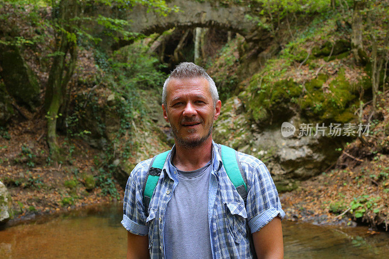 成年男子徒步旅行在美丽的自然景观与小溪流在森林和老废弃的石桥上面