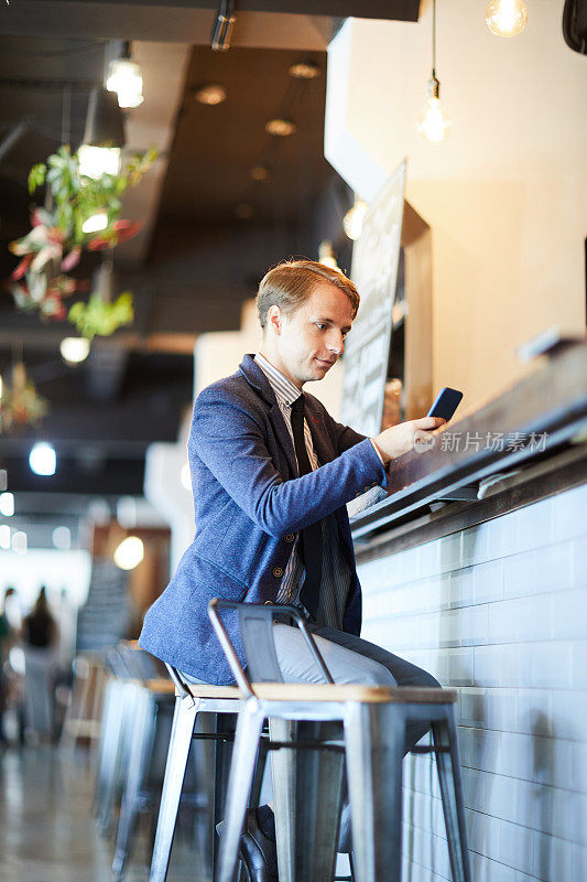 严肃的现代商务经理，穿着夹克坐在吧台边，边在咖啡馆休息边看手机短信