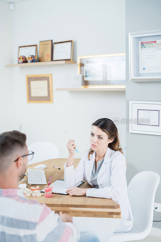 严肃沉思的女牙医穿着实验服坐在办公桌前，回答病人在办公室的问题