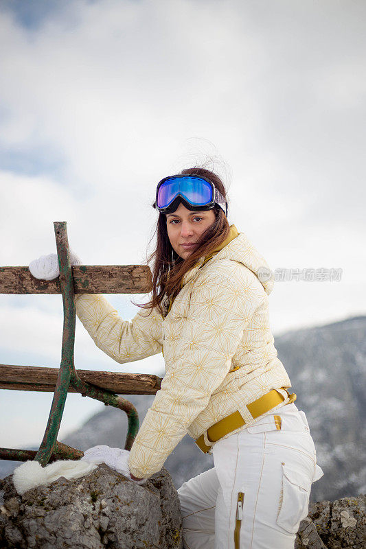 近景美丽的年轻女子在冬天的衣服站在一边，手拿木棍的背景雪山