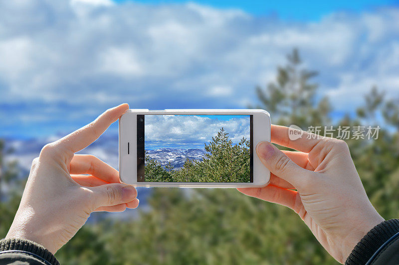 女孩拿着手机，用两只手拍着山谷的照片
