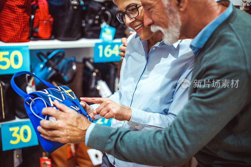一对老年夫妇在一家手提包和饰品店一起看一个蓝色的小手提包