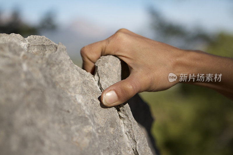 年轻女子攀岩者双手攀爬在悬崖峭壁上