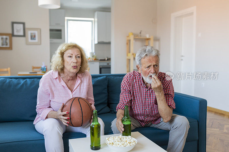 老夫妇在家里的沙发上看篮球比赛。