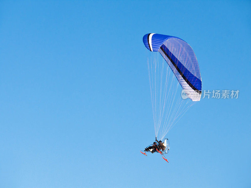 人在滑翔伞上飞行，有马达的滑翔伞。车辆在晴朗的蓝天。