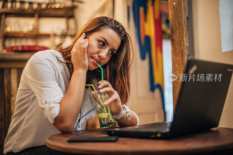 年轻女子喝着苏打水，用着笔记本电脑