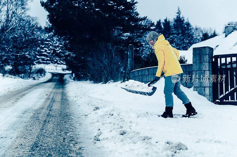 老妇人正在用雪铲清理积雪