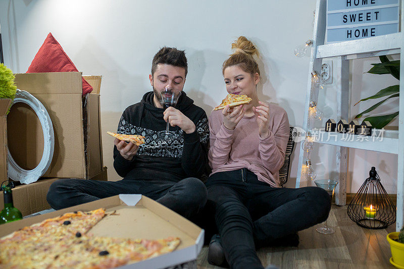 镜头中，年轻夫妇坐在地板上，吃着披萨，讨论着把盒子里的东西放在哪里