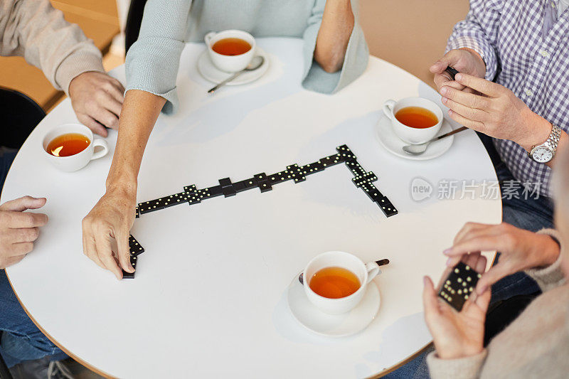 一群面目全非的老年人围坐在圆桌旁，拿着茶杯，在玩多米诺骨牌游戏上浪费时间