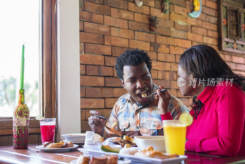 一对有着黝黑皮肤和非洲式发型的拉丁夫妇正在一家漂亮的餐馆里吃着典型的哥伦比亚食物