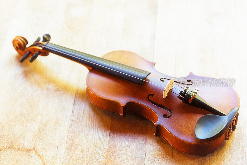 漂亮的旧小提琴躺在阳光下的木地板上