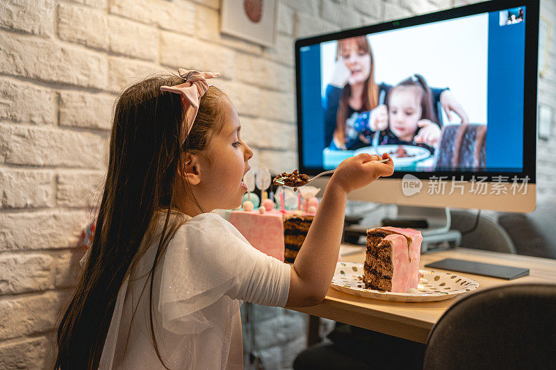 迷人的生日女孩吃生日蛋糕，同时与她的家人通过视频通话应用程序在家庭隔离