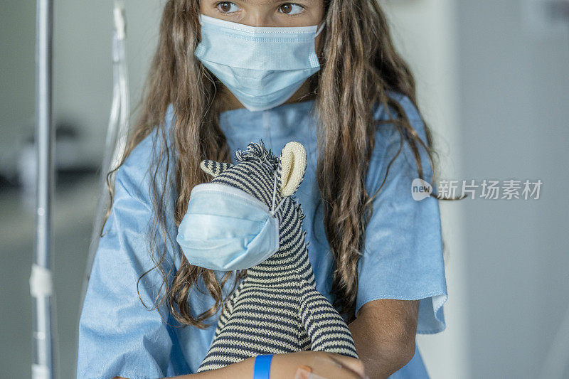 小女孩和她的毛绒动物在一个保护面罩在医院