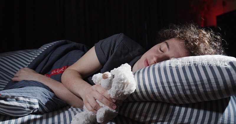 一个女人抱着一只泰迪熊在床上睡觉