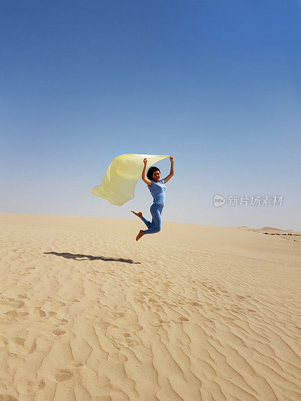 一个年轻女子在沙漠的沙子上跳。