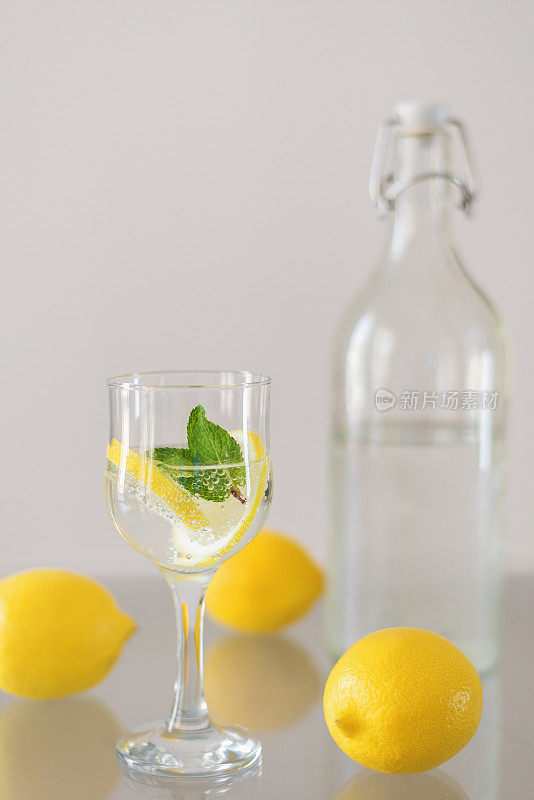 一瓶清凉的苏打水，一杯加柠檬和薄荷的饮料，玻璃桌上放着整个柠檬。排毒鸡尾酒