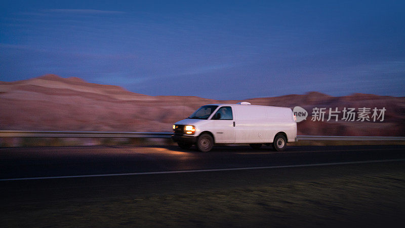 日落时分，一辆白色的货车行驶在美国的乡村道路上