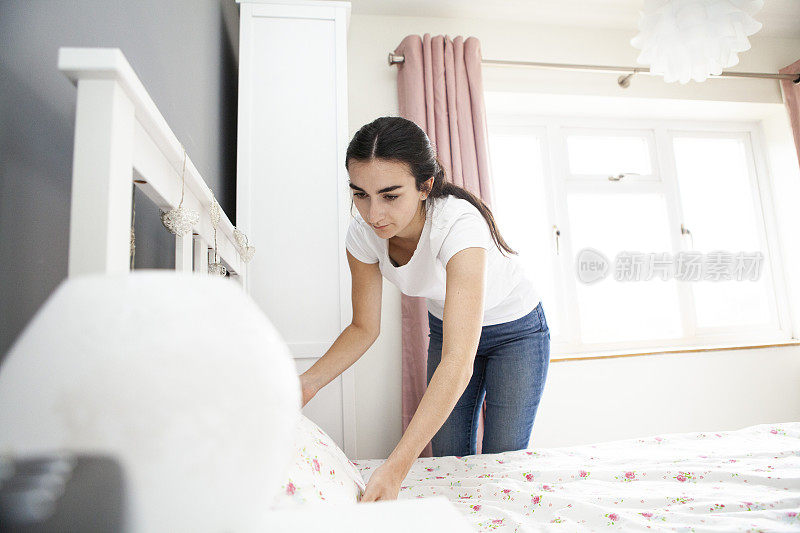 一个十几岁的女人在明亮的卧室里铺床