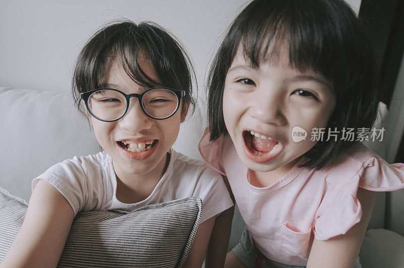 年轻的亚裔中国女孩在客厅的沙发上用平板电脑和他们的父亲愉快地聊天