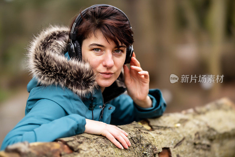 一个穿着蓝色雨衣的年轻女子坐在公园的长椅上，戴着耳机听音乐