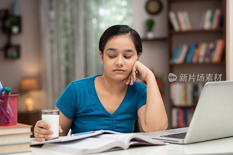 一个十几岁的女学生在家学习时喝牛奶的照片:库存照片