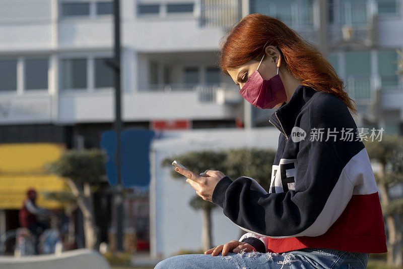 年轻女性戴着防护口罩在街上预防冠状病毒和防雾霾，使用智能手机的肖像