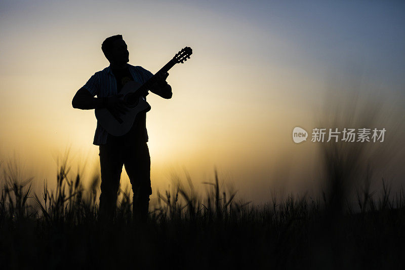 男性音乐家的剪影弹吉他在日落的背景