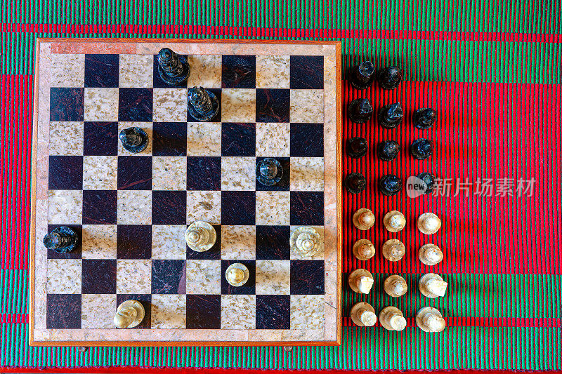 平放图像显示正在进行的象棋游戏。棋子由石头雕刻而成，棋盘上镶嵌着黑白有色的石头