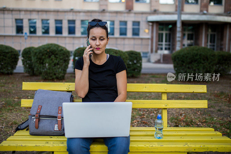 坐在长椅上使用笔记本电脑的女人
