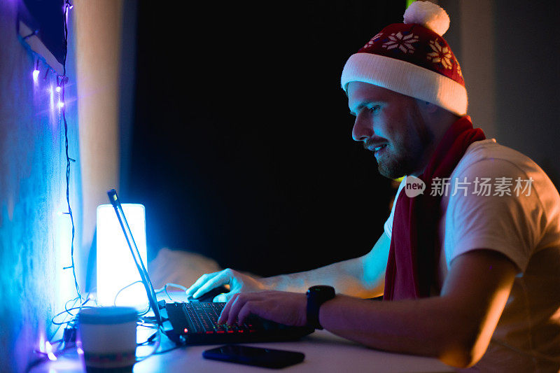 圣诞男性肖像，蓄着大胡子的男人戴着红色的圣诞帽，用笔记本电脑视频通话，庆祝新年的概念。室内摄影与人，帽和电脑