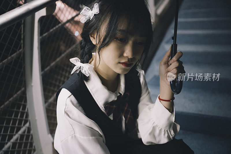 成都，一名年轻的亚洲女子打着伞，夜晚坐在一座桥上