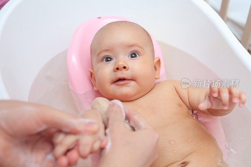妈妈用海绵的手在浴室里给宝宝洗澡