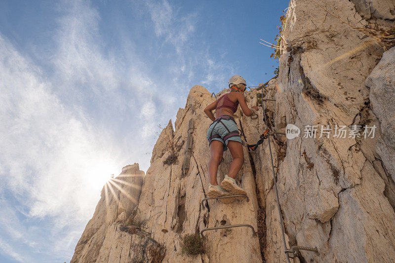 女性攀岩者爬上梯子到达岩石顶部的低角度视图
