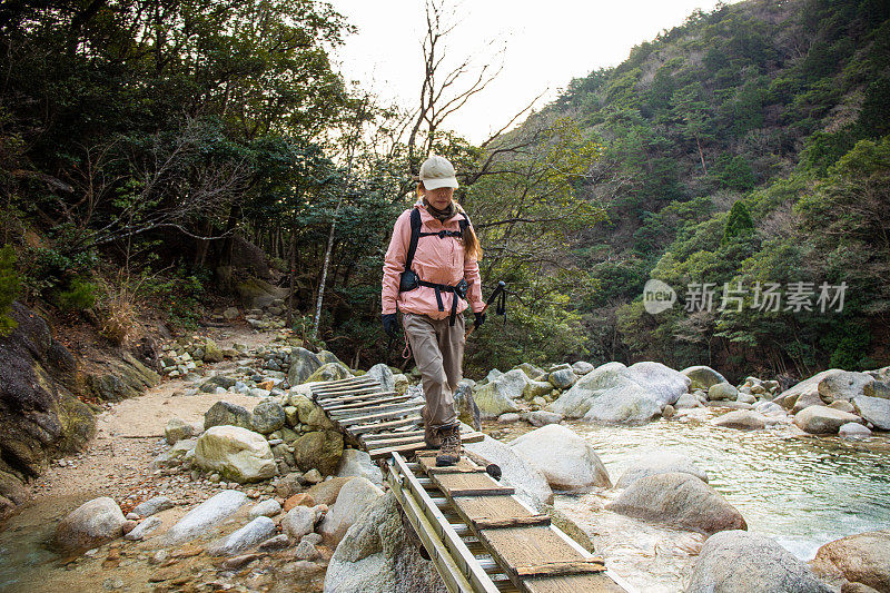 一位女登山客穿过小溪上的木桥