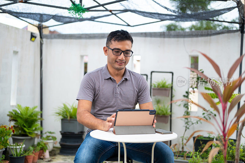 中年穆斯林男子在前院花园用数码平板电脑工作