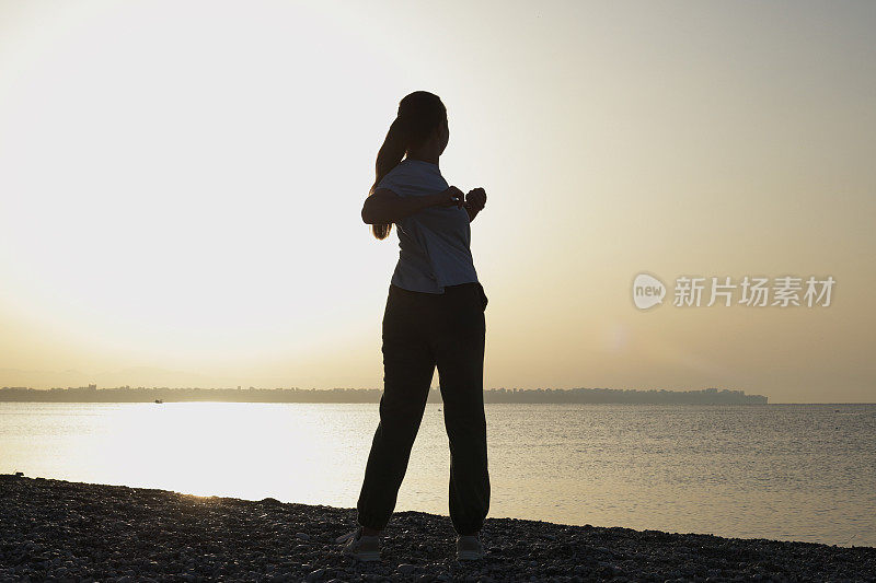 年轻女子在海边做晨练，以在日出时保持身材
