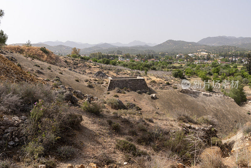 位于干旱山坡上的历史黄金加工遗址的蓄水池，背景是村庄和山脉