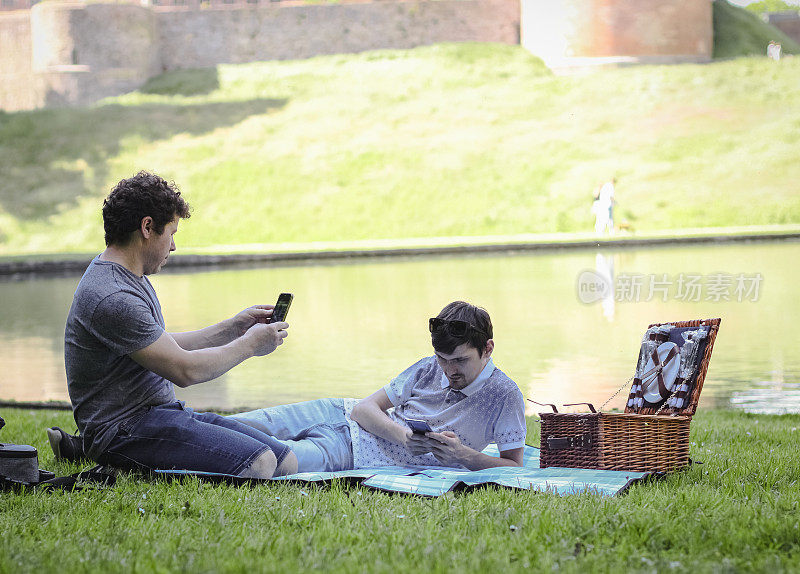 两个英俊的白人年轻人坐在铺开的床罩上使用手机
