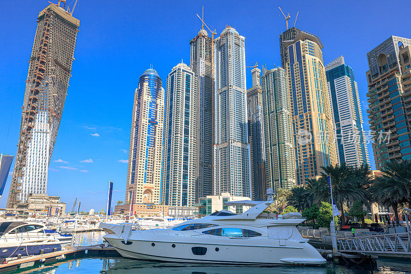 阿拉伯联合酋长国迪拜——透过停泊在迪拜码头的船只，望向高高的海滨摩天大楼，映衬着湛蓝的清晨天空。