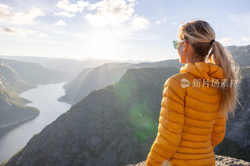 一名女子站在挪威峡湾的顶端，凝视着日落时壮观的景色