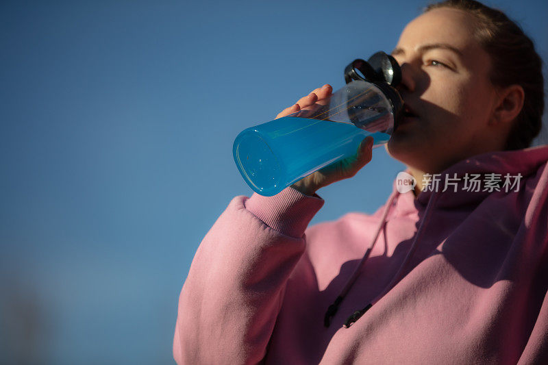 年轻女子在户外运动期间在外面补水。