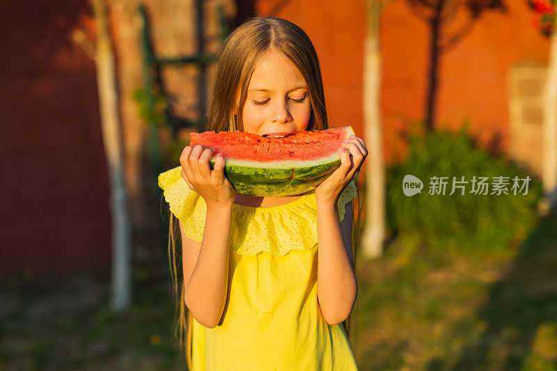 快乐的金发女孩穿着黄色的衣服，拿着一块西瓜。夏天的生活方式。的童年。