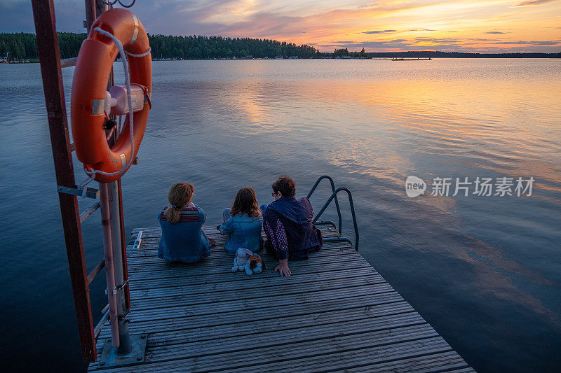 女人，一个老妇人，一个年轻的女人和一个8岁的女孩，一个高加索家庭花时间在一起，看美丽的日落，欣赏风景。在湖上的木码头上。