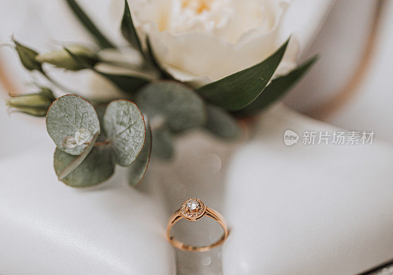 白色背景上，镶有钻石的金婚戒，旁边是绿色的玫瑰。照片中的婚礼细节。