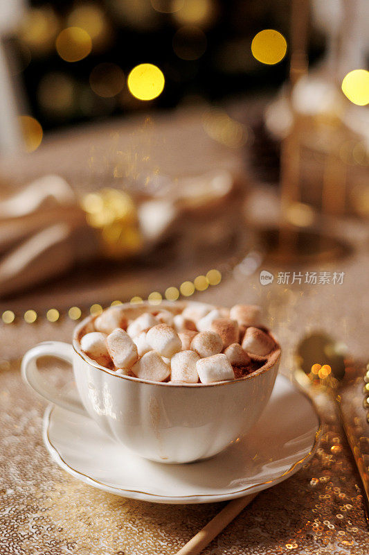经典经典的白色波兹兰杯与碟子与可可和棉花糖在金色闪闪发光的桌布。圣诞或新年节日宴会豪华餐桌设置。背景上的花环灯散景。
